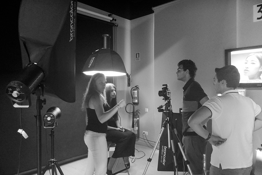 Fotografía en blanco y negro de una sesión de fotos en estudio, mostrando a un equipo de personas utilizando equipos de iluminación profesional Broncolor y una modelo frente a la cámara.