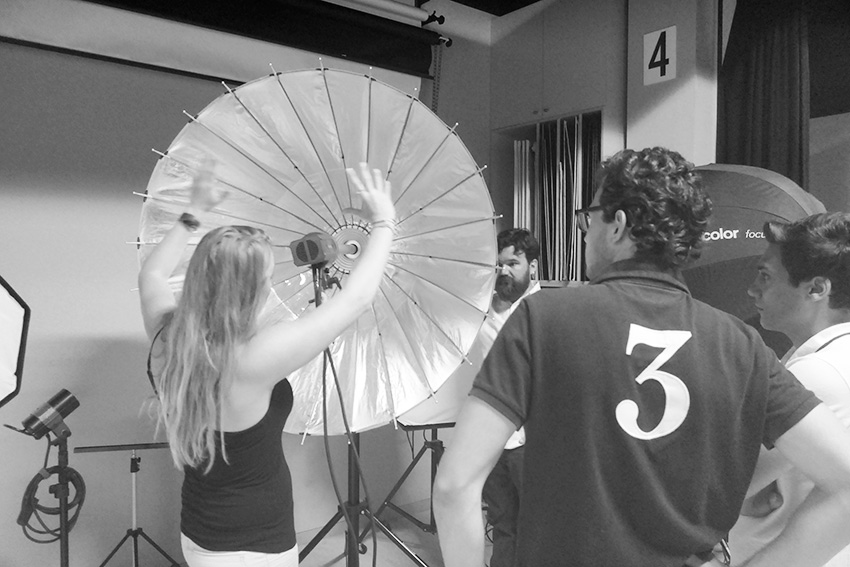 Equipo de fotógrafos ajustando un reflector Broncolor en un estudio, preparándose para una sesión fotográfica, capturado en blanco y negro.