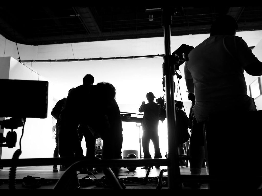 Siluetas de un equipo de producción en un estudio trabajando con equipos de iluminación y cámaras de vídeo, capturando la esencia del trabajo en equipo y la técnica detrás de la creación de contenido visual de calidad.