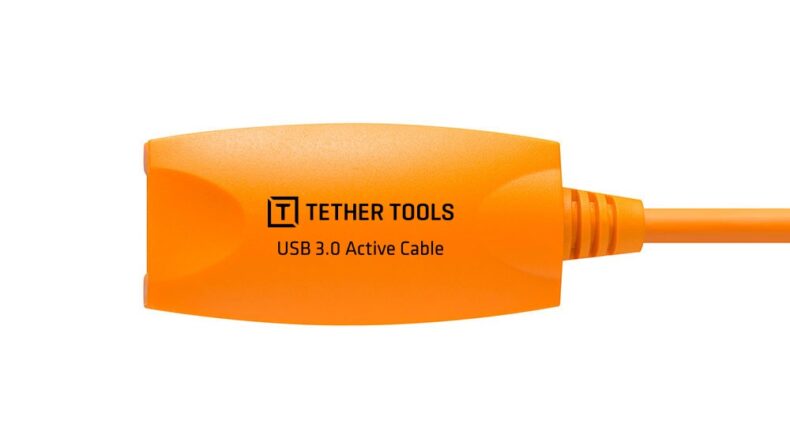 Detalle de un repetidor de cable USB 3.0 Activo de Tether Tools en color naranja, optimizado para uso en equipos profesionales de fotografía y vídeo, mostrado sobre fondo blanco.